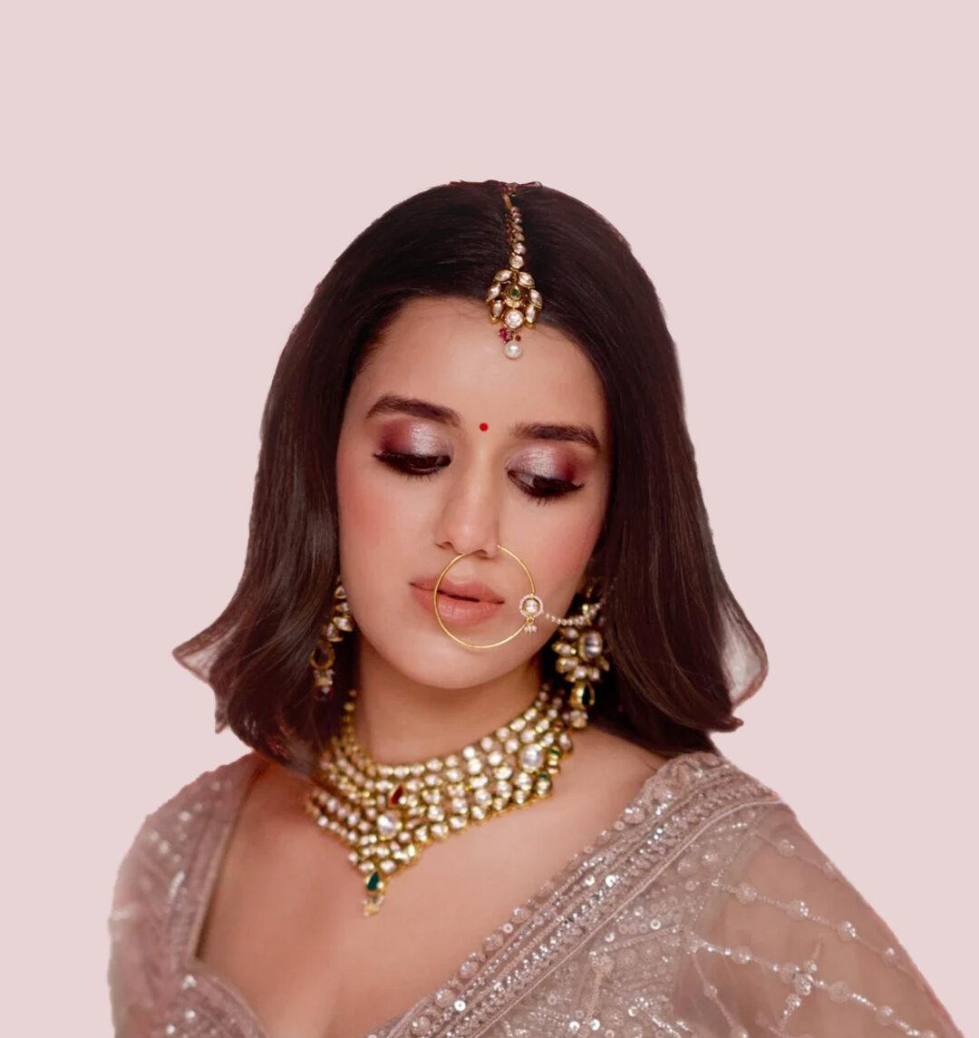 Close-up of bridal makeup with mauve smoky eyes, nath, kundan necklace, maang tikka, and sleek bob by Bellance Salon