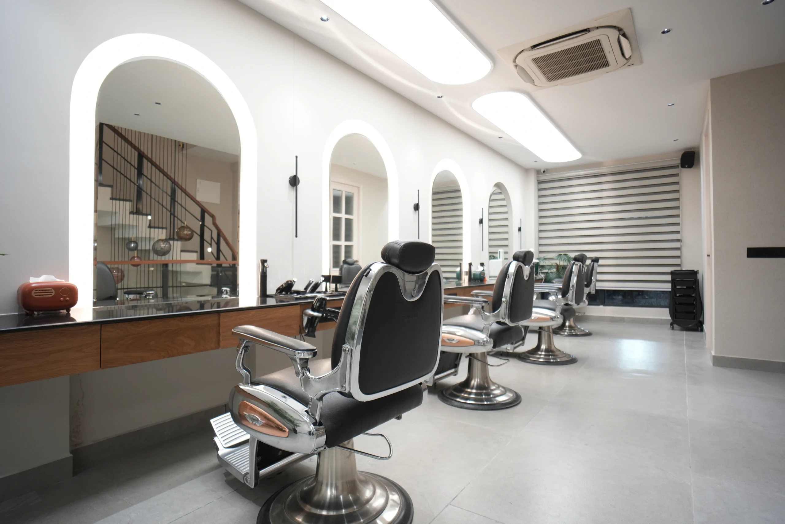 Bellance Salon men's grooming area with chrome barber chairs, arched mirrors reflecting staircase, and wooden vanity